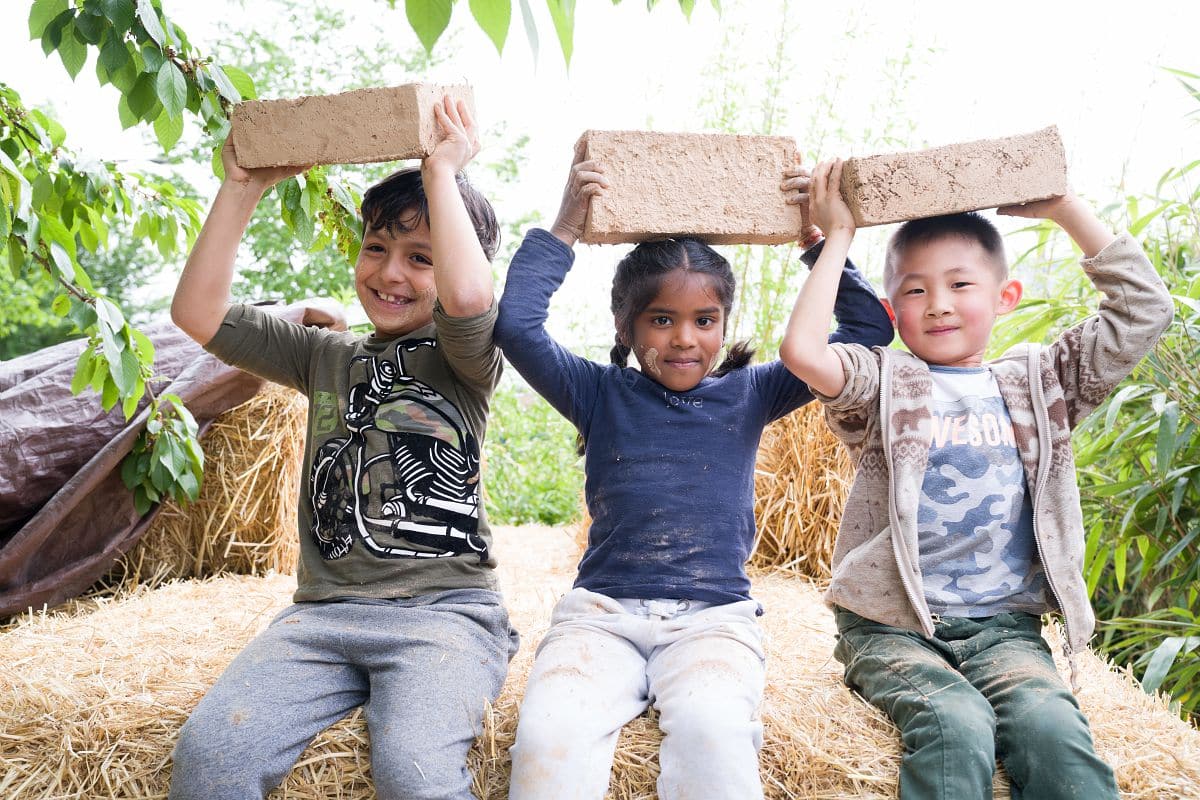 Des enfants tiennent des briques de terre crue.